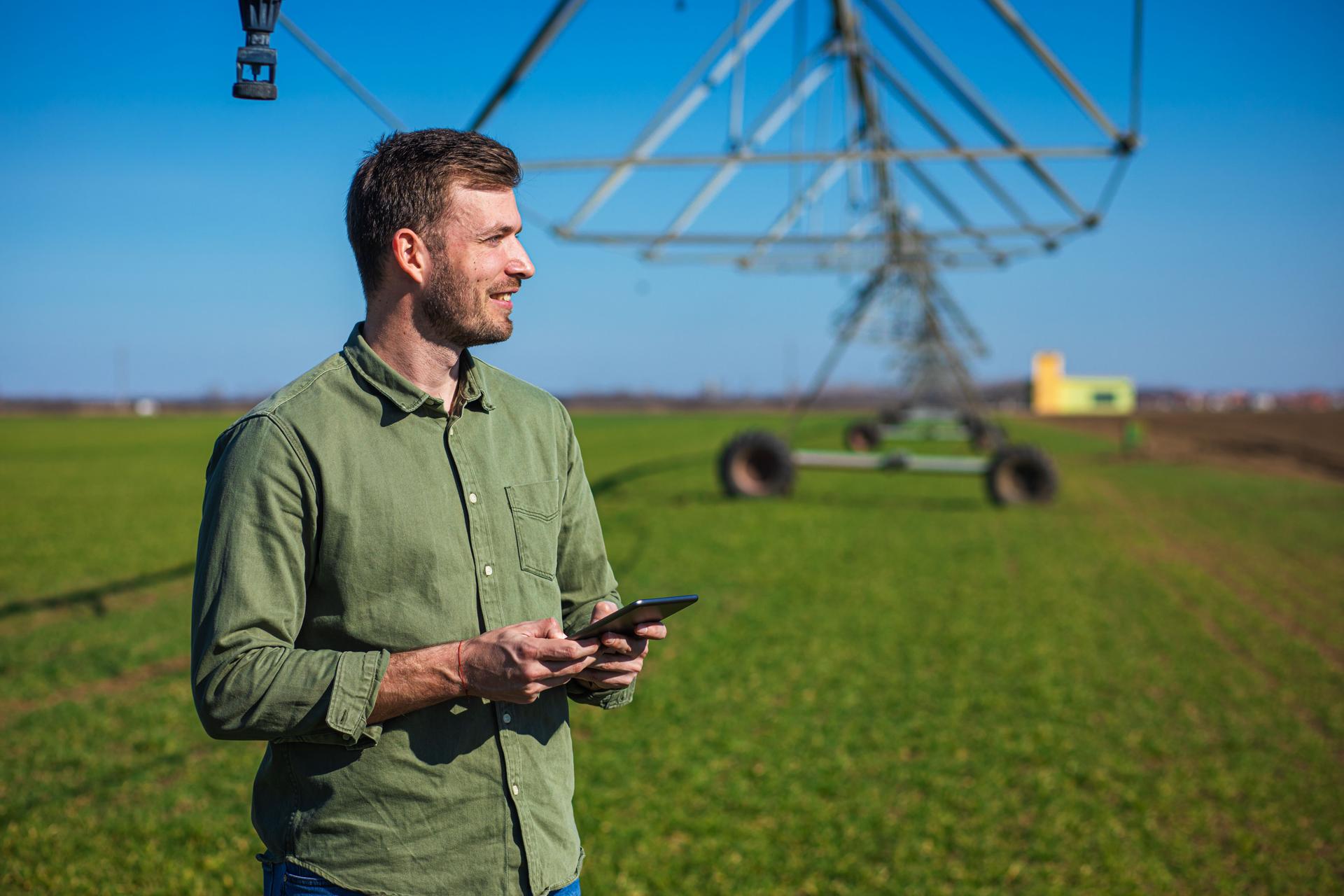 Young farmer standing in wheat field and setup irrigation system on tablet.