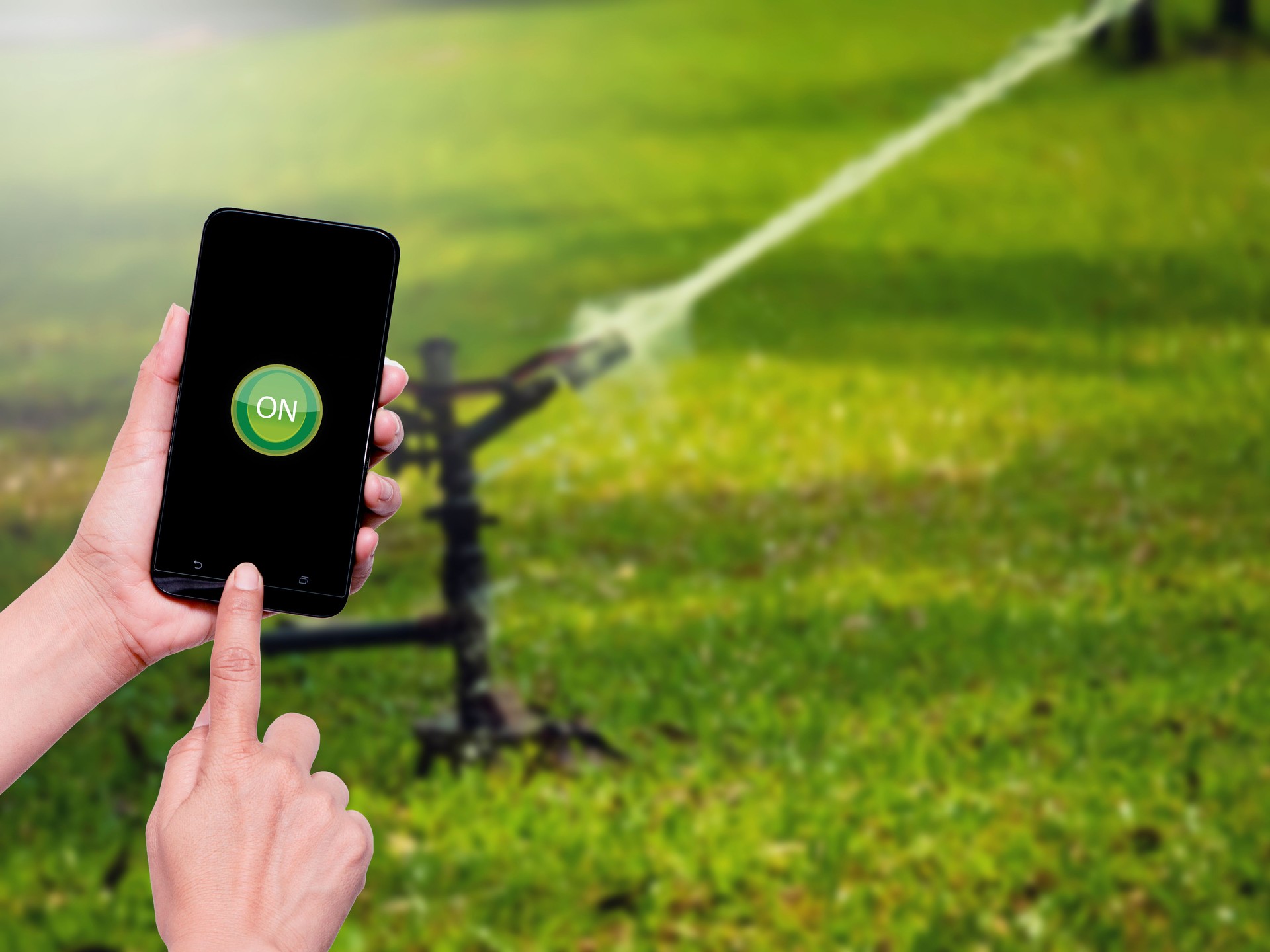 Woman hand holding the mobile phone with button ON  icon on screen for automatic water control system in agriculture